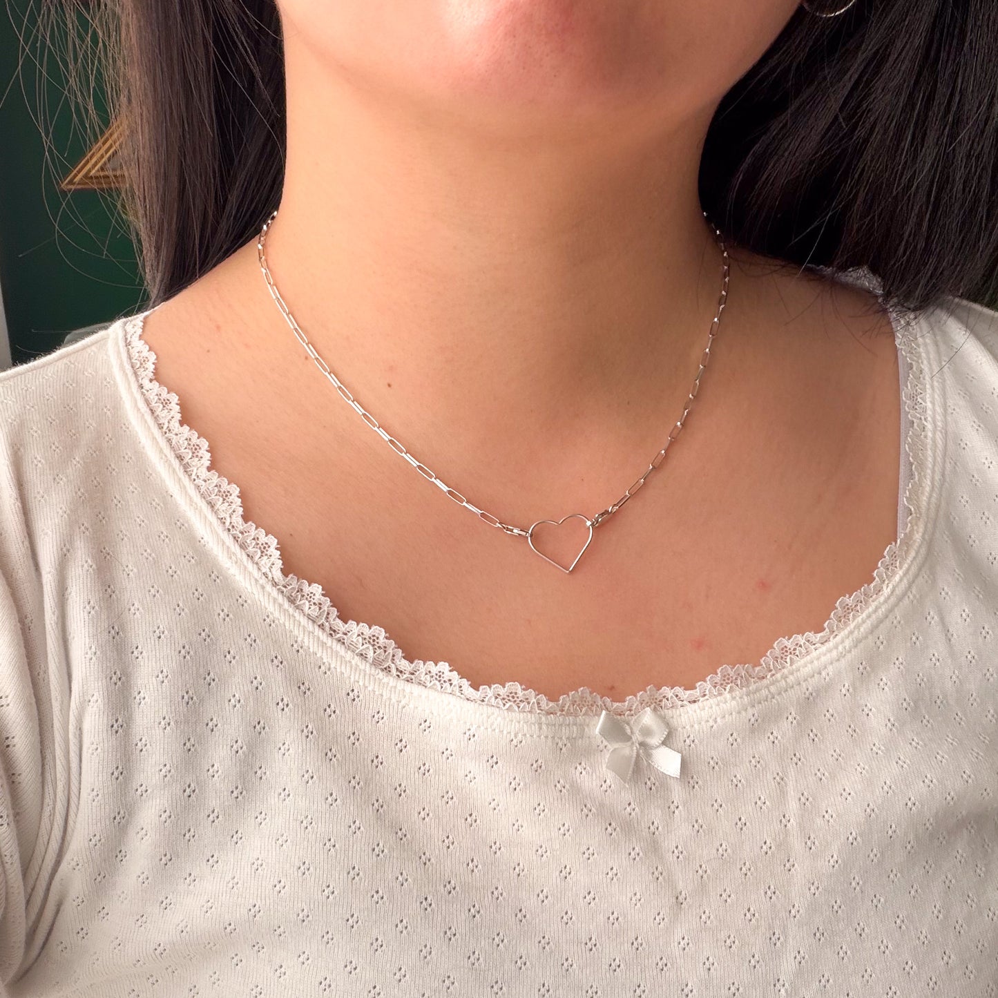 Close-up of a person wearing a white top with lace trim and a silver necklace with a heart pendant.
