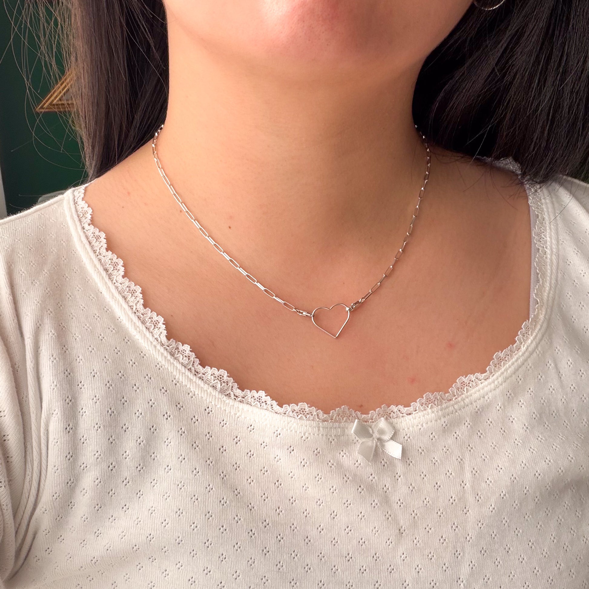 Close-up of a person wearing a white top with lace trim and a silver necklace with a heart pendant.