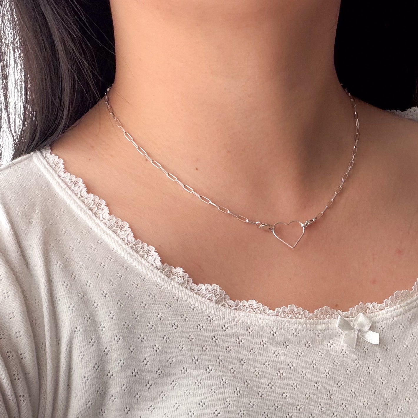 Silver necklace with a heart pendant worn by a person in a white top.